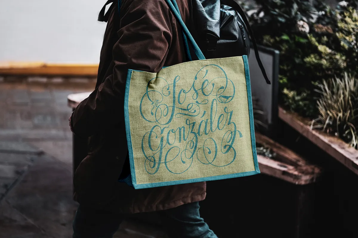 Tote bag naturel porté à l'épaule par quelqu'un dont on ne voit pas le visage. Sur le tote bag est imprimé le lettrage rendant hommage à José Gonzalez