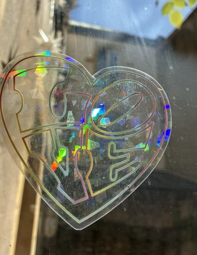 Suncatcher Love accroché sur une fenêtre : un autocollant qui attrape les arc-en-ciel en forme de coeur.